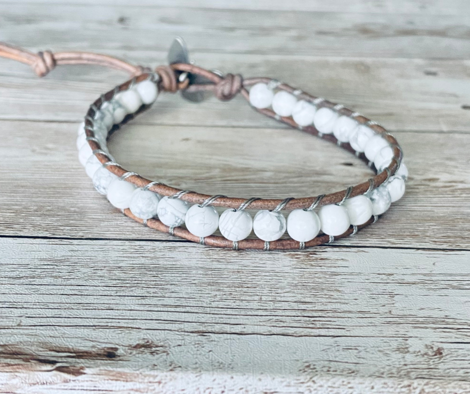 A wrap ankle bracelet featuring white gemstone beads and natural gray leather. The anklet has a gray button clasp.  The design can wrap around the ankle one time.  The anklet is displayed on a light wood surface.