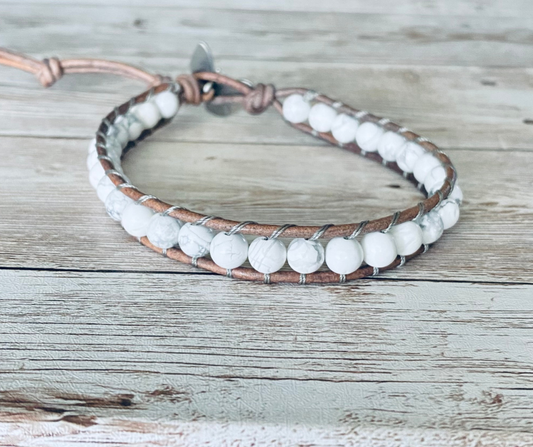 A wrap ankle bracelet featuring white gemstone beads and natural gray leather. The anklet has a gray button clasp.  The design can wrap around the ankle one time.  The anklet is displayed on a light wood surface.