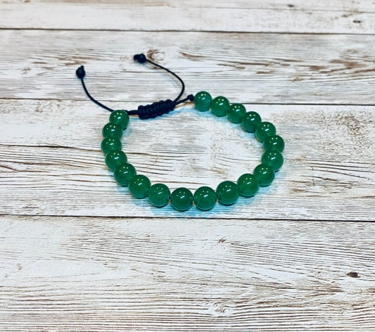 A beaded bracelet made with round green aventurine gemstone beads on an adjustable black nylon cord, with small beads at the ends of the nylon cord.   It is displayed on a light wood background.
